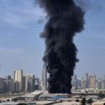 Composite news graphic showing explosions over the skylines of Dubai, Abu Dhabi, and Doha, with missile interceptions lighting up the night sky and air raid sirens sounding in Tel Aviv during escalating Middle East conflict.